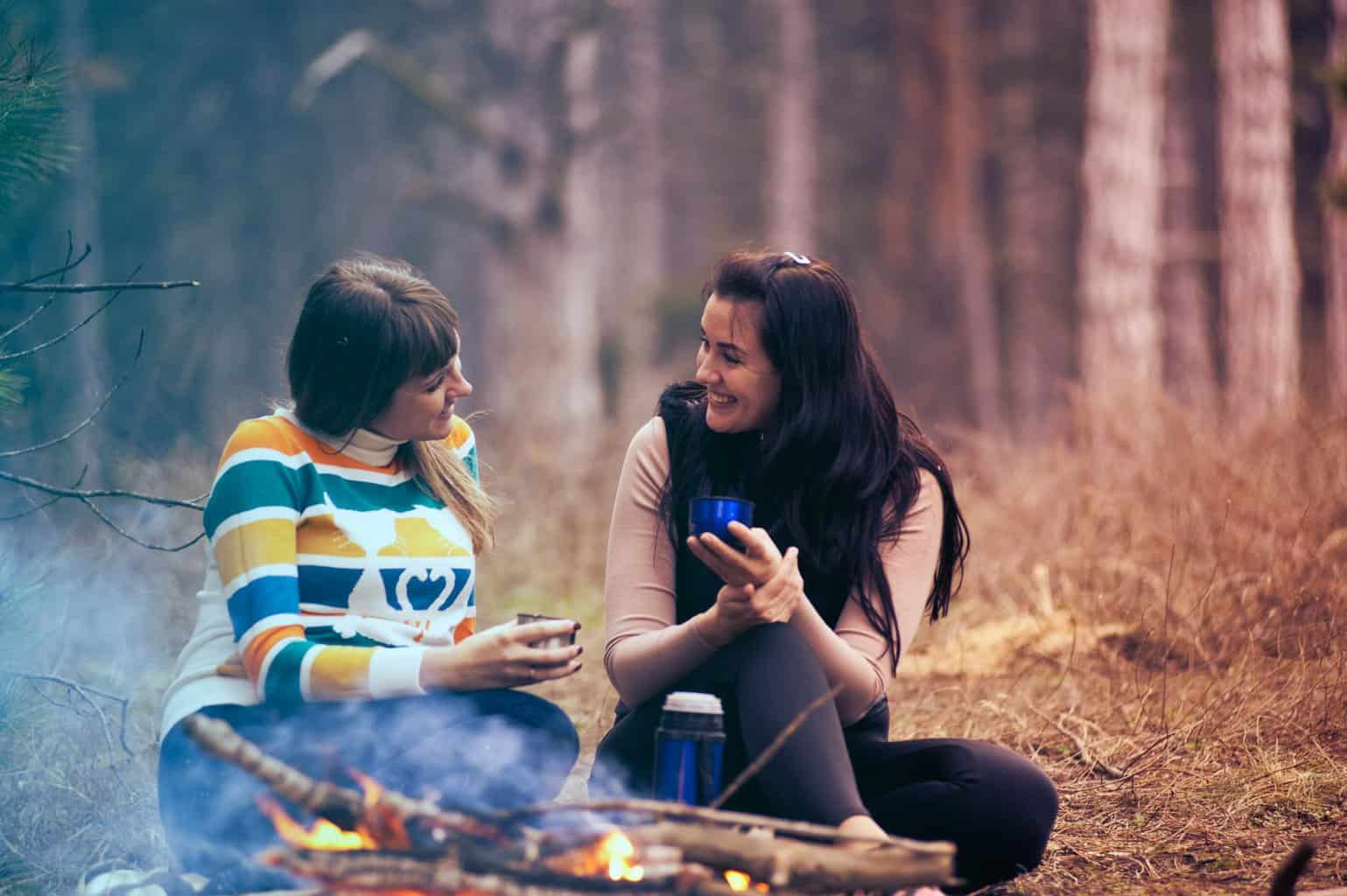two women sitting on ground near bonfire/giving
