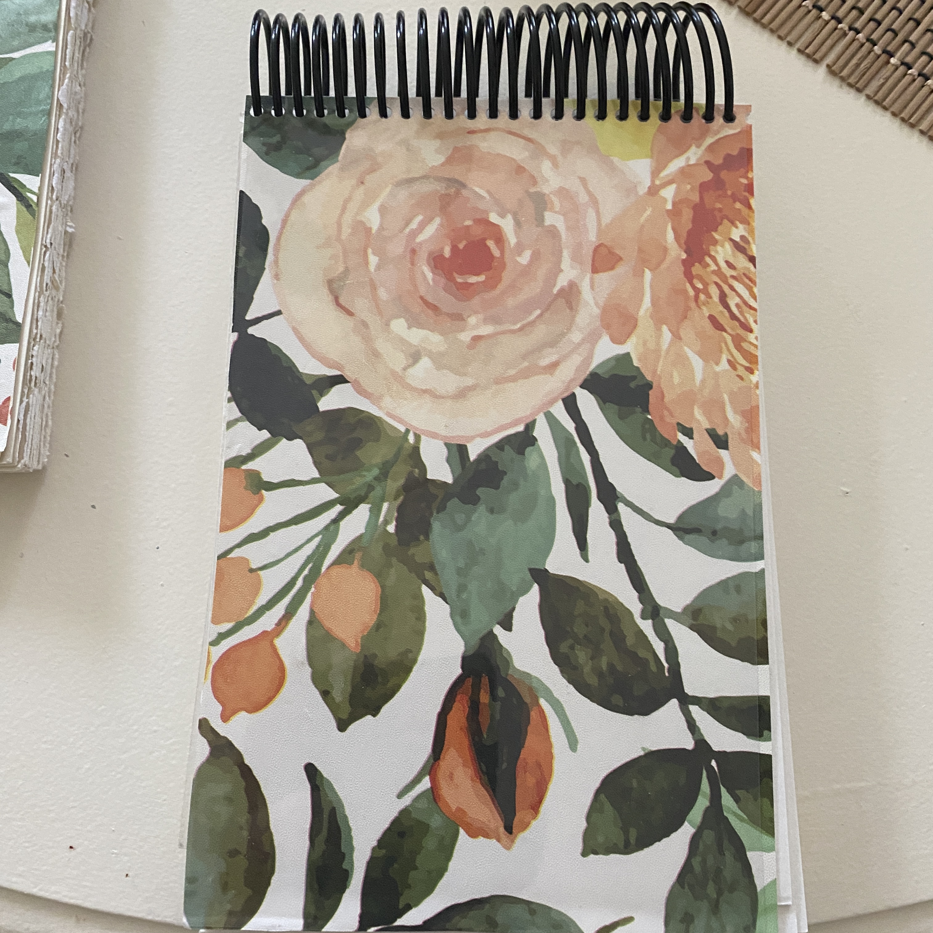 A spiral-bound notebook with a floral cover design featuring watercolor illustrations of roses and green leaves.