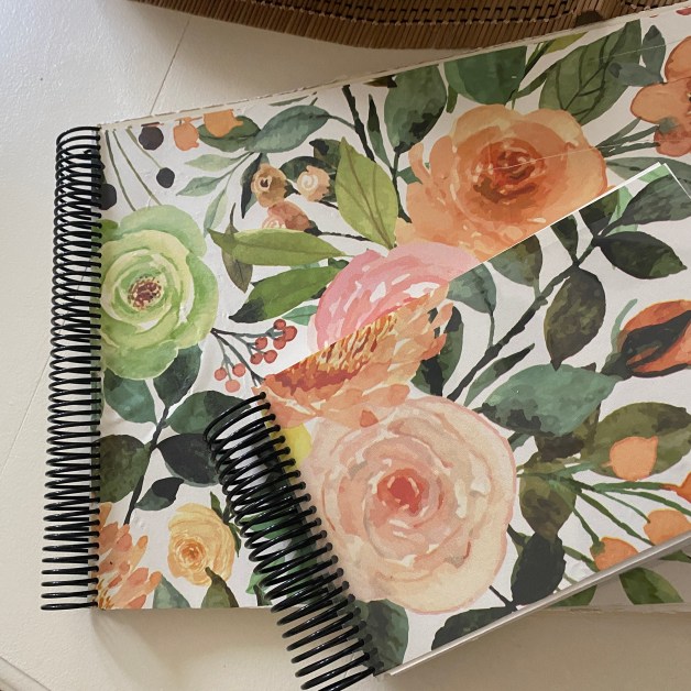 Notebook with a floral watercolor design featuring a variety of flowers and leaves, resting on a white surface.