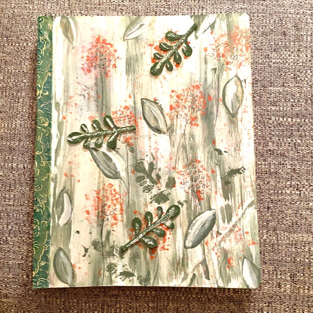 Journal with a floral design on a faux-wood background lying on a linen-textured surface. The spine of the journal features a green ornate pattern.