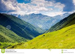 landscapes-2 | goodthoughtsgoodlives Lush green hills in the foreground leading into rugged mountain peaks with patches of snow under a partly cloudy sky.