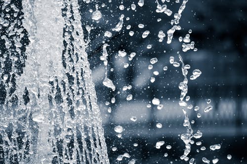 Close-up photograph of water splashing, with detailed droplets captured in midair against a blurred background/grieving