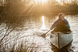 canoe | goodthoughtsgoodlives A person paddling a canoe on a calm river at sunset, with the sunlight creating a reflective pathway on the water./anxiety