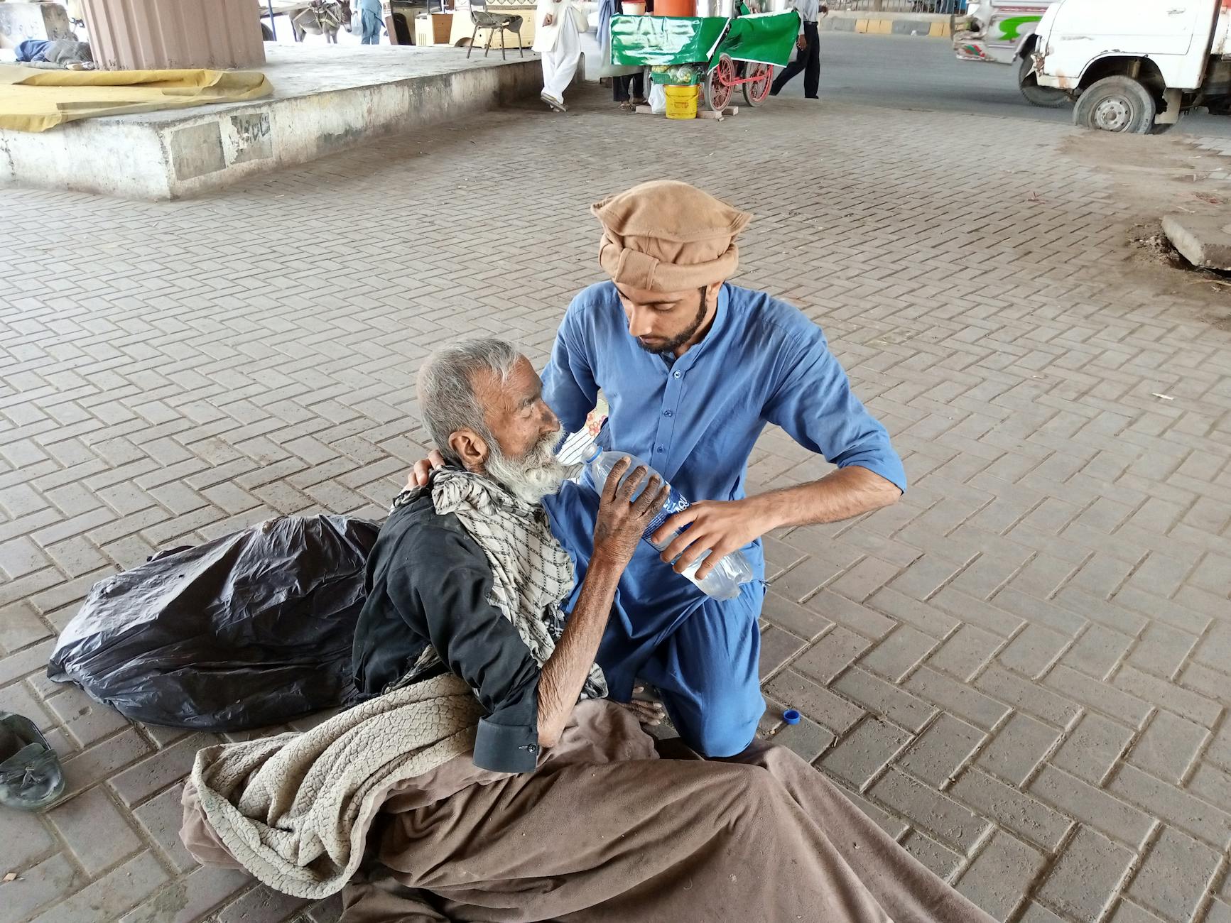 man in blue clothing feeding an old man/conduct