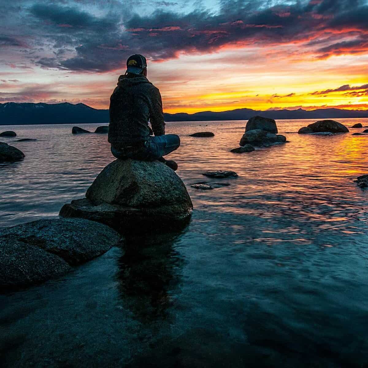 person sitting on rock on body of water