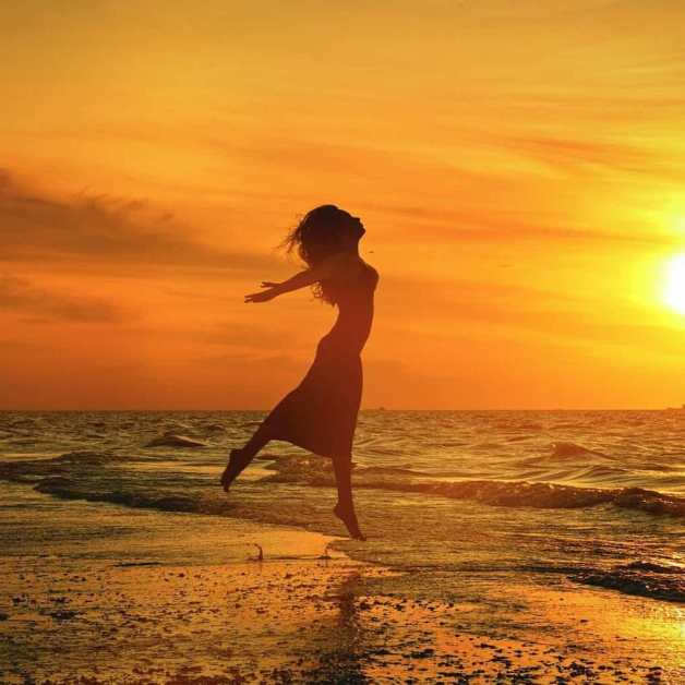 silhouette of unrecognizable woman jumping above sea beach at sunset