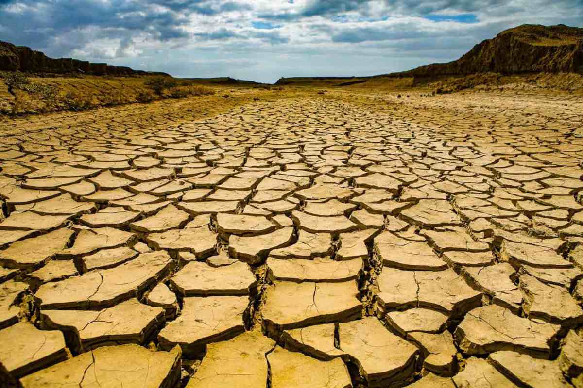 Parched desert ground with large cracked earth stretching to distant hills under a cloudy sky