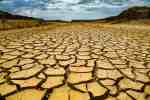 Parched desert ground with large cracked earth stretching to distant hills under a cloudy sky