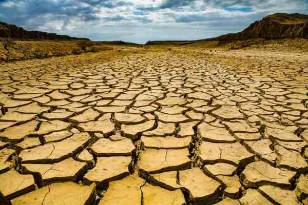 Parched desert ground with large cracked earth stretching to distant hills under a cloudy sky