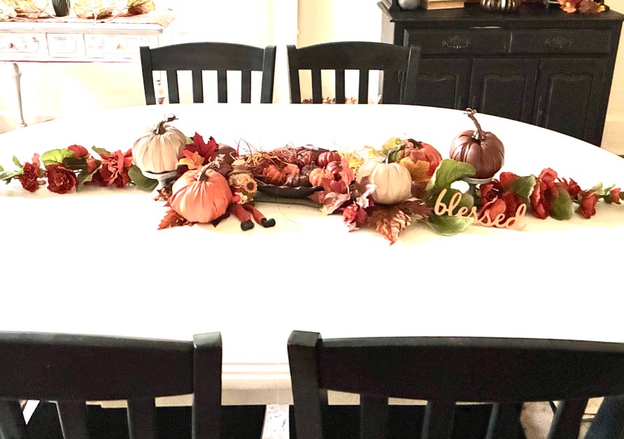 img_5909 | goodthoughtsgoodlives White dining table decorated with small pumpkins, autumn leaves, and a'blessed' sign; black chairs around the table and a dark cabinet in the background.