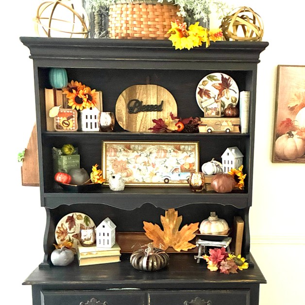 img_5917 | goodthoughtsgoodlives Fall-themed display on a black shelf: pumpkins, sunflowers, leaves, wicker baskets and miniature houses.