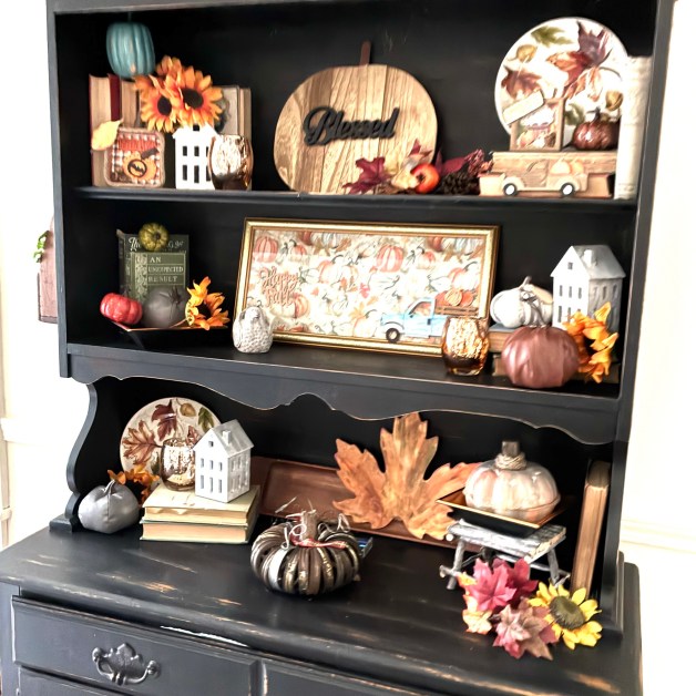 img_5918 | goodthoughtsgoodlives Fall-themed shelf display with pumpkins, sunflowers, leaves, and a round wooden 'Blessed' sign surrounded by small houses and decor pieces.