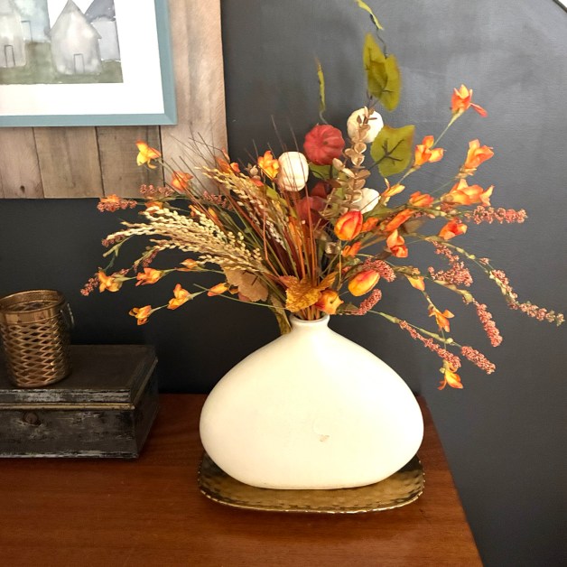 img_6017-1 | goodthoughtsgoodlives White ceramic vase with an orange and cream fall floral arrangement on a wooden table against a dark blue wall.